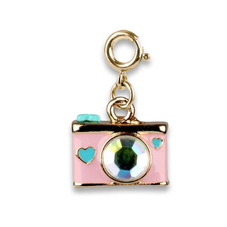 A pink camera charm with gold-tone metal trim, a large iridescent rhinestone in the center, and two small turquoise heart accents, attached to a gold clasp on a white background.