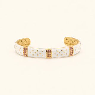 White cuff bracelet with gold accents and pink stones on a beige background