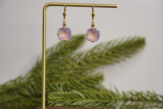 Gold earrings with purple gemstones on a stand with green leaves in the background