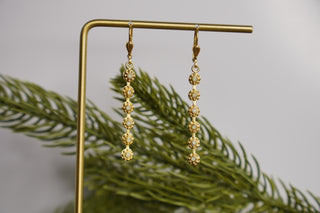 Gold earrings on a stand with green leaves in the background