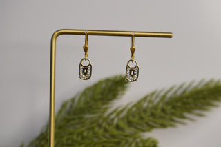 Gold earrings on a stand with a blurred green plant in the foreground