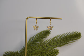 Gold butterfly earrings on a stand with a green leafy background