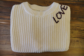 Folded beige sweater with 'LOVE' text on a wooden surface