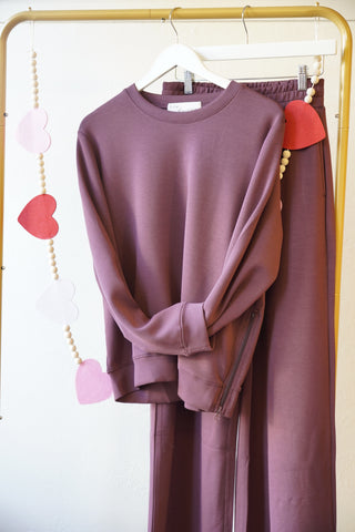 Maroon sweatshirt hanging on rack with maroon sweatpants on white background