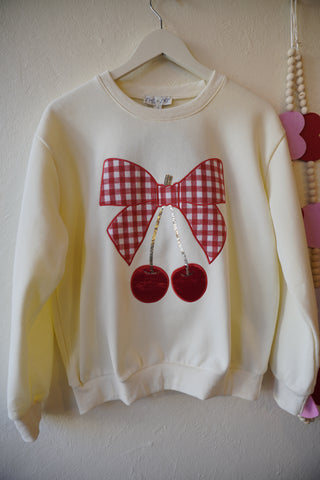 White sweatshirt with red and pink checkered bow and cherries on a light background