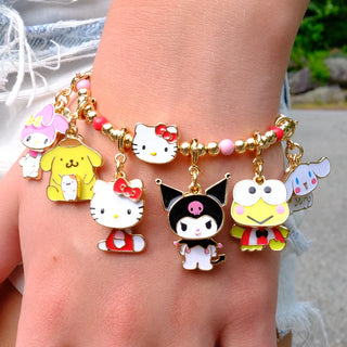 A close-up of a gold charm bracelet worn on a wrist, featuring multiple Sanrio character charms including Hello Kitty, Kuromi, Pompompurin, and Keroppi, accented with pink and white beads.