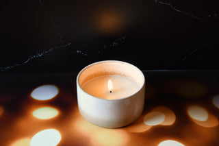 Candle in a white container on a dark surface with light reflections