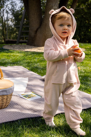 Child in a pink bear costume standing on grass with a picnic blanket and basket.