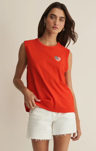 Woman wearing a red sleeveless top with a small flag design and white shorts on a beige background