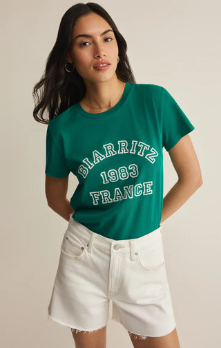 Woman wearing a green t-shirt with 'BIARRITZ 1983 FRANCE' text on a beige background