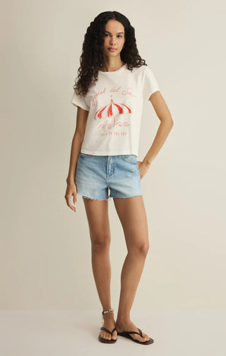 Woman wearing a white t-shirt with a graphic design and denim shorts on a plain background