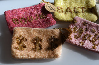 Four textured pouches with embroidered text and dollar signs on a light background