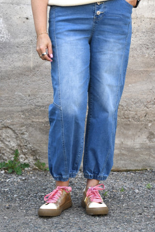 Person wearing blue jeans and pink sneakers on a concrete surface.