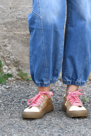 Person wearing blue jeans and beige sneakers with pink laces on a stone surface.