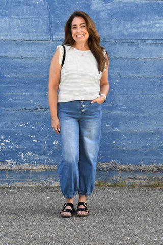 Woman wearing a white striped shirt and blue jeans standing against a blue wall.