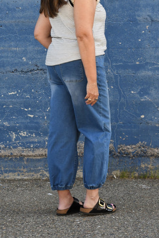 Person wearing a striped top and blue pants against a blue wall.