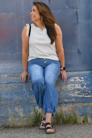Woman sitting on a stone ledge wearing a striped tank top and blue jeans against a blue wall.