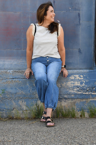 Woman sitting on a blue wall wearing a striped shirt and jeans.