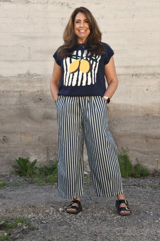 Woman wearing a navy t-shirt with lemon design and striped pants standing against a concrete wall.