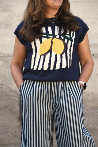 Person wearing a navy blue top with lemon design and striped pants against a stone wall.
