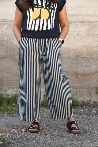 Person wearing a navy sleeveless top with lemon design and black and white striped pants against a stone wall.
