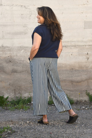 Woman wearing a navy top and striped pants standing against a textured wall.