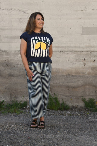 Woman wearing a navy t-shirt with a lemon design and striped pants standing against a concrete wall.