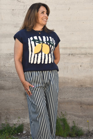 Woman wearing a navy blue t-shirt with lemon design and striped pants against a concrete wall.