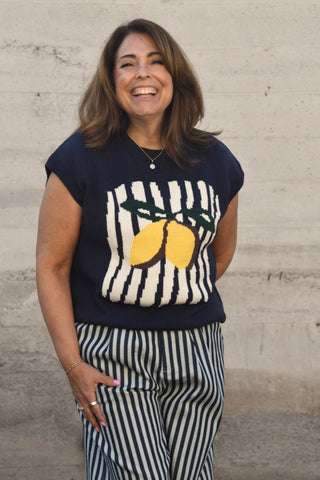 Woman wearing a navy sweater with lemon design and striped pants against a beige wall.