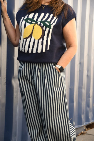 Person wearing a navy sweater with lemon design and striped pants against a blue wall.