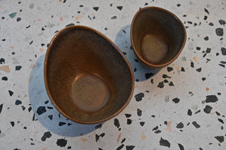 Two brown ceramic bowls on a speckled surface