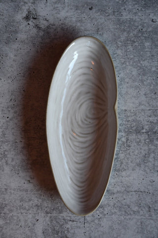 White ceramic dish with wavy pattern on a gray concrete surface