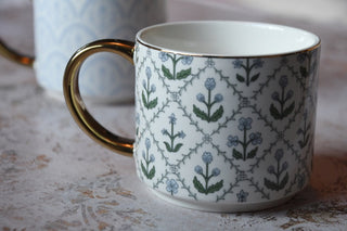 White mug with floral pattern and gold handle on a textured surface
