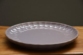 A round ceramic plate with a scalloped, wavy rim, shown on a wooden surface against a dark gray background.
