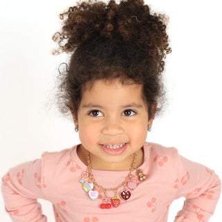 Child wearing a pink shirt with heart patterns and multiple necklaces on a white background
