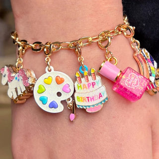 Bracelet with colorful charms including a unicorn, paint palette, birthday cake, and nail polish bottle on a wrist.