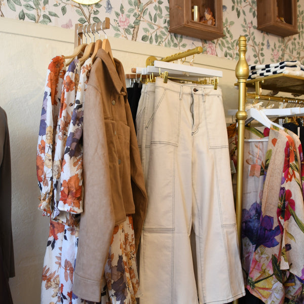 Clothing rack with various garments against a floral wallpapered wall.