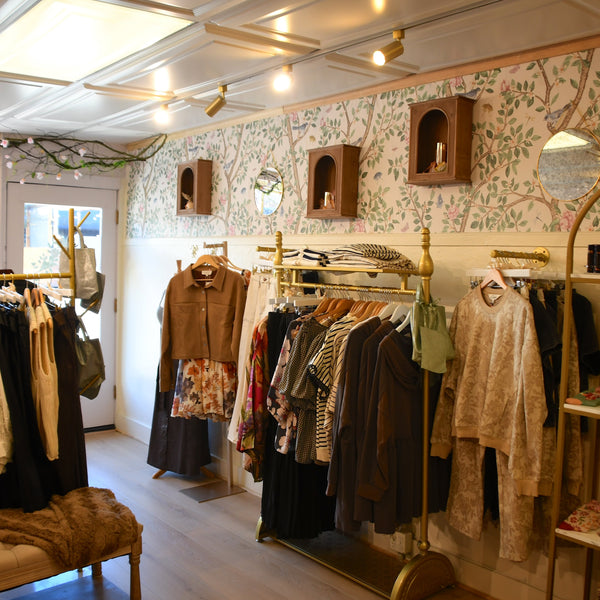 Clothing store interior with racks of clothes and floral wallpaper.