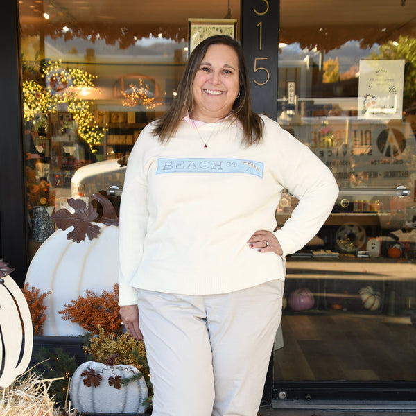 Woman standing in front of a store with decorative pumpkins and hay bales.
