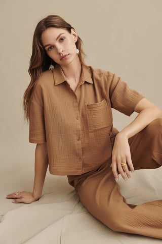 Woman wearing a brown textured shirt and pants sitting on a light-colored floor.