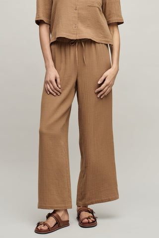 Person wearing a brown outfit with wide-leg pants on a plain background