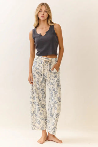 Woman wearing a dark tank top and floral pants on a plain background