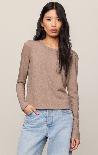 Woman wearing a brown long-sleeve top and light blue jeans against a beige background