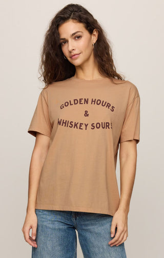 Woman wearing a tan t-shirt with text, standing against a plain background