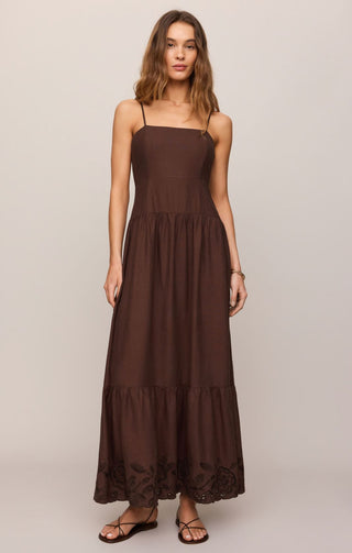 Woman wearing a brown dress with lace details on a plain background