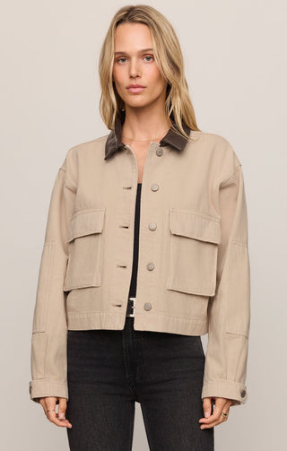 Woman wearing a beige jacket with dark collar and buttons on a plain background