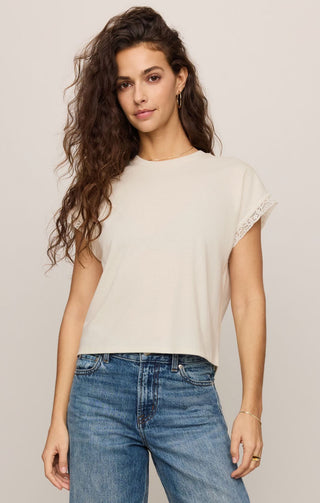 Woman wearing a beige t-shirt and blue jeans against a plain background
