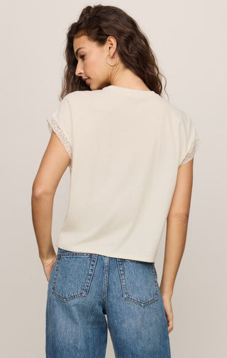 Woman wearing a beige top and blue jeans against a plain background