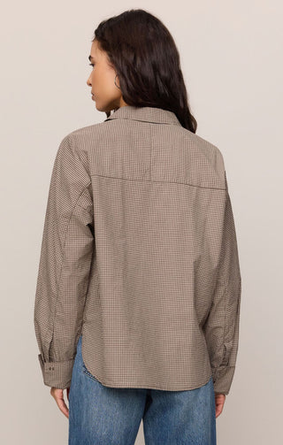 Woman wearing a brown checkered shirt and blue jeans against a beige background