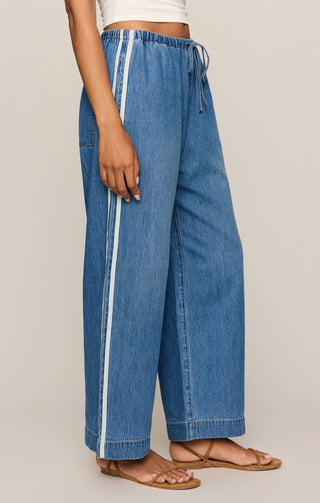 Blue denim pants with a white stripe on a neutral background